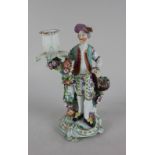 A Derby porcelain figural candlestick modelled as a gentleman flower seller beside a basket of