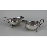 A pair of George V silver sauce boats shaped borders and scroll handle on three shell and hoof feet,