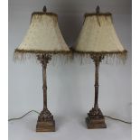A pair of bronze effect column table lamps on square bases, gold fabric shades with beaded trim,