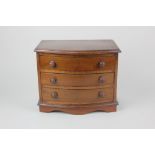 A miniature mahogany bow front chest of three drawers with turned knob handles on bracket feet