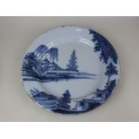 An 18th century English Delft blue and white charger decorated with a river landscape, verso paper