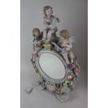 A Sitzendorf porcelain table mirror encrusted with flowers and mounted with three cherubs, on scroll
