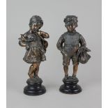 A pair of metal figures of a boy and a girl with copper patina, both on circular ebonised base