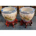 A pair of modern Oriental ceramic jardineres on wooden stands, each decorated with peacocks and