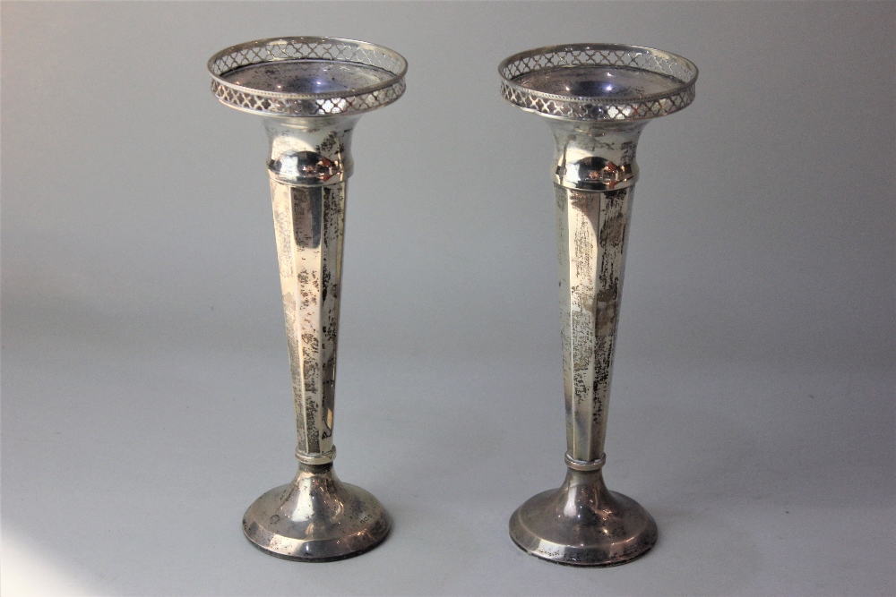 A pair of George V silver vases with pierced rims on facetted tapered stems and loaded circular