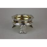 A George IV silver circular salt with cast floral border and gilt interior on three feet shaped as