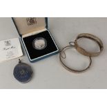 An oval silver locket with engraved initials 'DM', two silver hinged bangles (one gold plated),