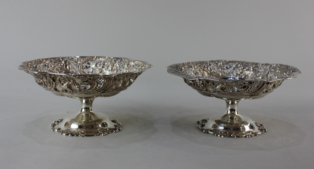 A pair of sterling silver pedestal dishes with lobed centres and floral and scroll embossed