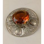 A Scottish plaid brooch with large amber coloured claw set centre and circular border with embossed