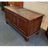 An oak coffer with hinged two panel lid above carved three panel front on stile supports 106cm