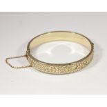 A 9ct gold hinged bangle with engraved decoration, 12g