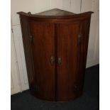 A George III mahogany bowfront wall hanging corner cupboard with two panel doors enclosing three