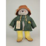 A Paddington Bear teddy bear by Gabrielle Design wearing a green duffle coat and yellow Dunlop