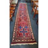 A Persian runner carpet red field with blue cross motifs within cream patterned border, 415cm by