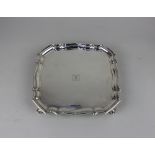 A George V silver salver square form with pie crust border on four scroll feet, central engraved