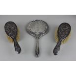 A pair of Chinese white metal dressing table brushes the backs embossed with figures in a garden,