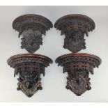 Two pairs of gothic carved wood wall brackets each with mask design and gilt embellishments, one