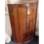 A George III oak bowfront hanging corner cupboard, with two panel doors flanked by reeded columns,