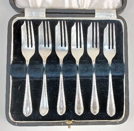 A cased set of six George V silver cake forks the handles with engraved borders, maker Cooper