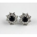 A pair of sapphire and diamond cluster ear studs each claw set with the circular cut sapphire in a