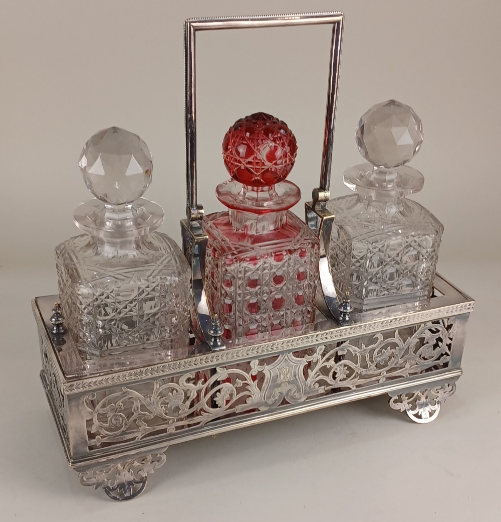 A silver plated three bottle tantalus with engraved initials and pierced scrolling foliate