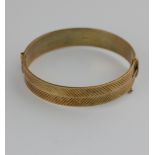 A 9ct gold oval hinged bangle the back and front with herringbone cut faceted decoration on a snap