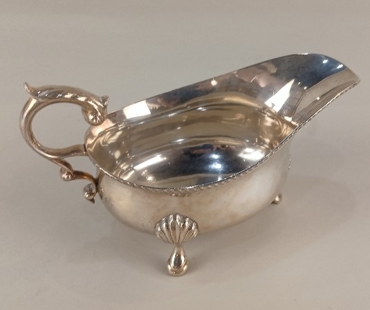 A George V silver sauce boat with flying scroll handle on three shell cabriole feet, maker