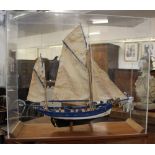 A painted wooden model of a two-masted sailing boat in a perspex display case case 72.5cm by 87cm