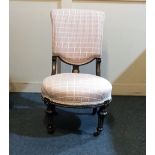 A Victorian ebonised nursing chair with upholstered back and circular seat on baluster legs and