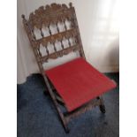A small carved folding chair with slung fabric seat, the back with floral carved cresting rail above