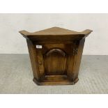 A SMALL OAK REPRODUCTION WALL MOUNTED CORNER CABINET.