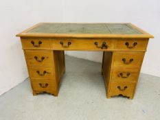 A REPRODUCTION PINE NINE DRAWER KNEE HOLE DESK, THE TOP WITH INSET TOOLED GREEN LEATHER - W 126CM.