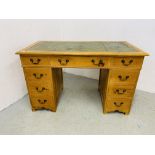 A REPRODUCTION PINE NINE DRAWER KNEE HOLE DESK, THE TOP WITH INSET TOOLED GREEN LEATHER - W 126CM.