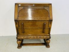 AN OAK 1930'S TWO DRAWER WRITING BUREAU WITH CARVED DETAIL AND BULBOUS FORE LEGS.