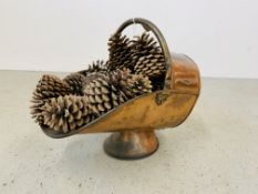 AN ANTIQUE COPPER COAL HELMET CONTAINING PINE CONES.