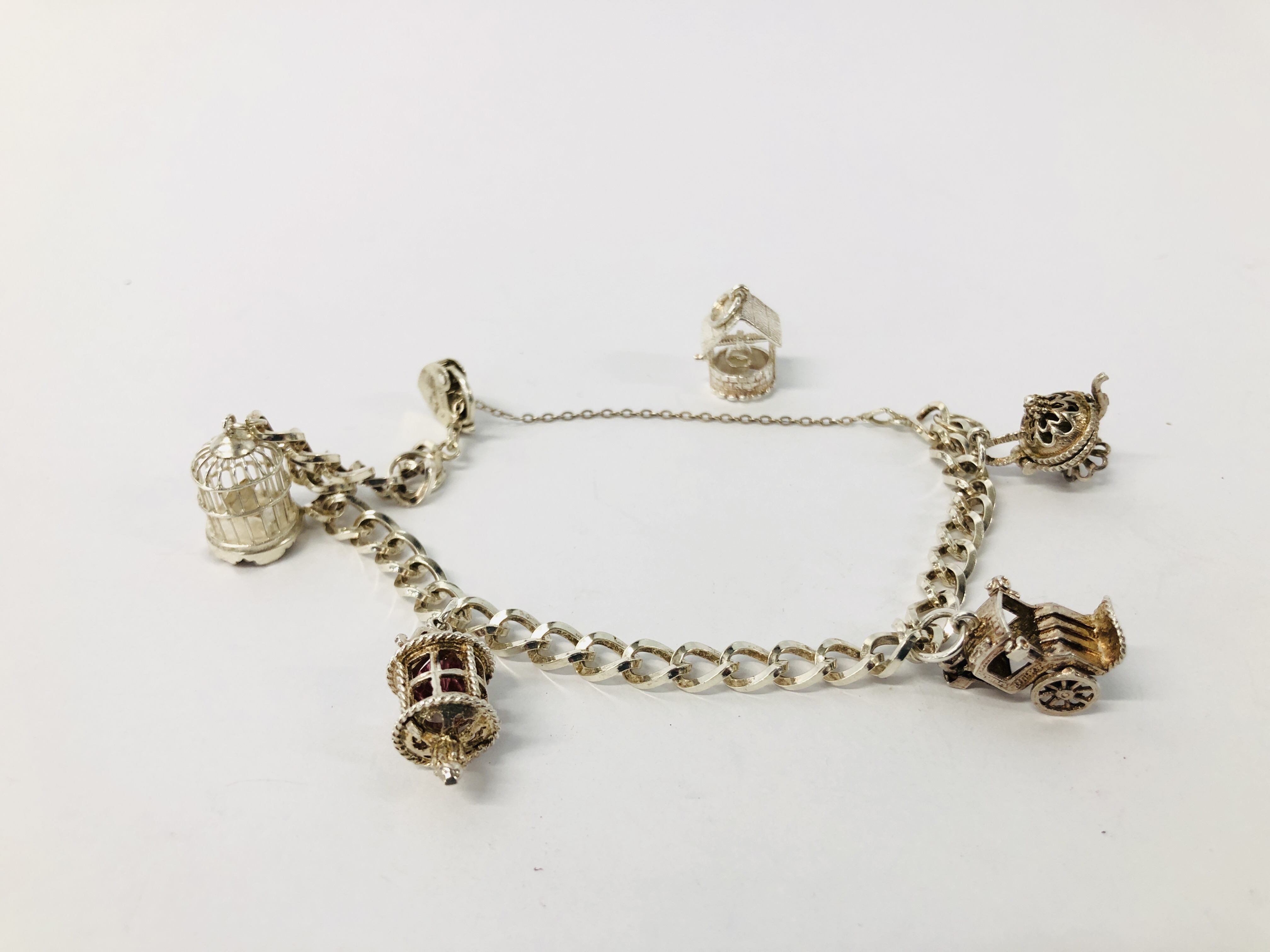 A SILVER CHARM BRACELET WITH FIVE ATTACHED CHARMS TO INCLUDE BIRD CAGE, WISHING WELL, CART ETC.