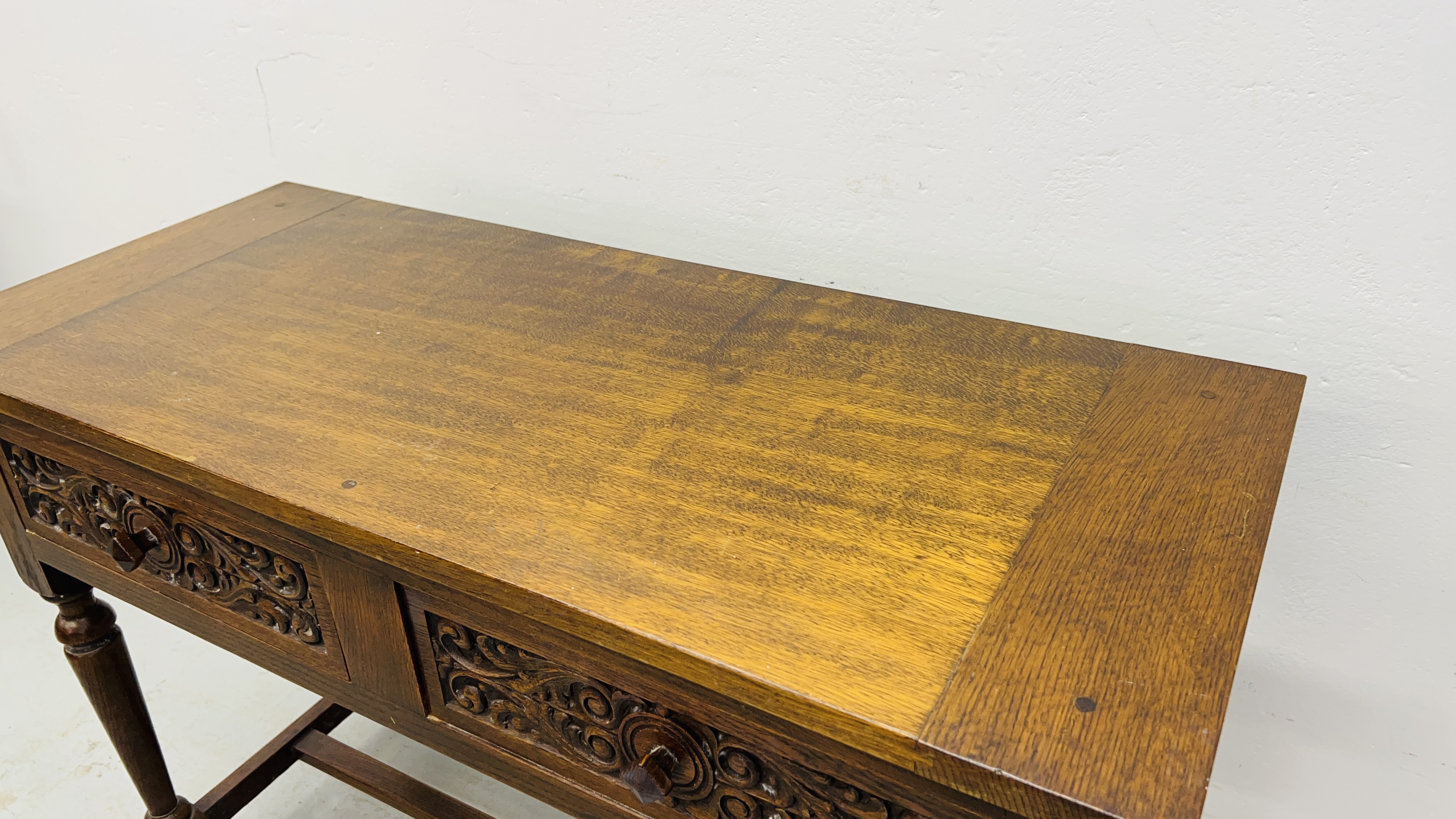 A REPRODUCTION SOLID OAK TWO DRAWER SIDE TABLE WITH CARVED DRAWER FRONTS W 107CM, D 46CM, H 77CM. - Image 7 of 9