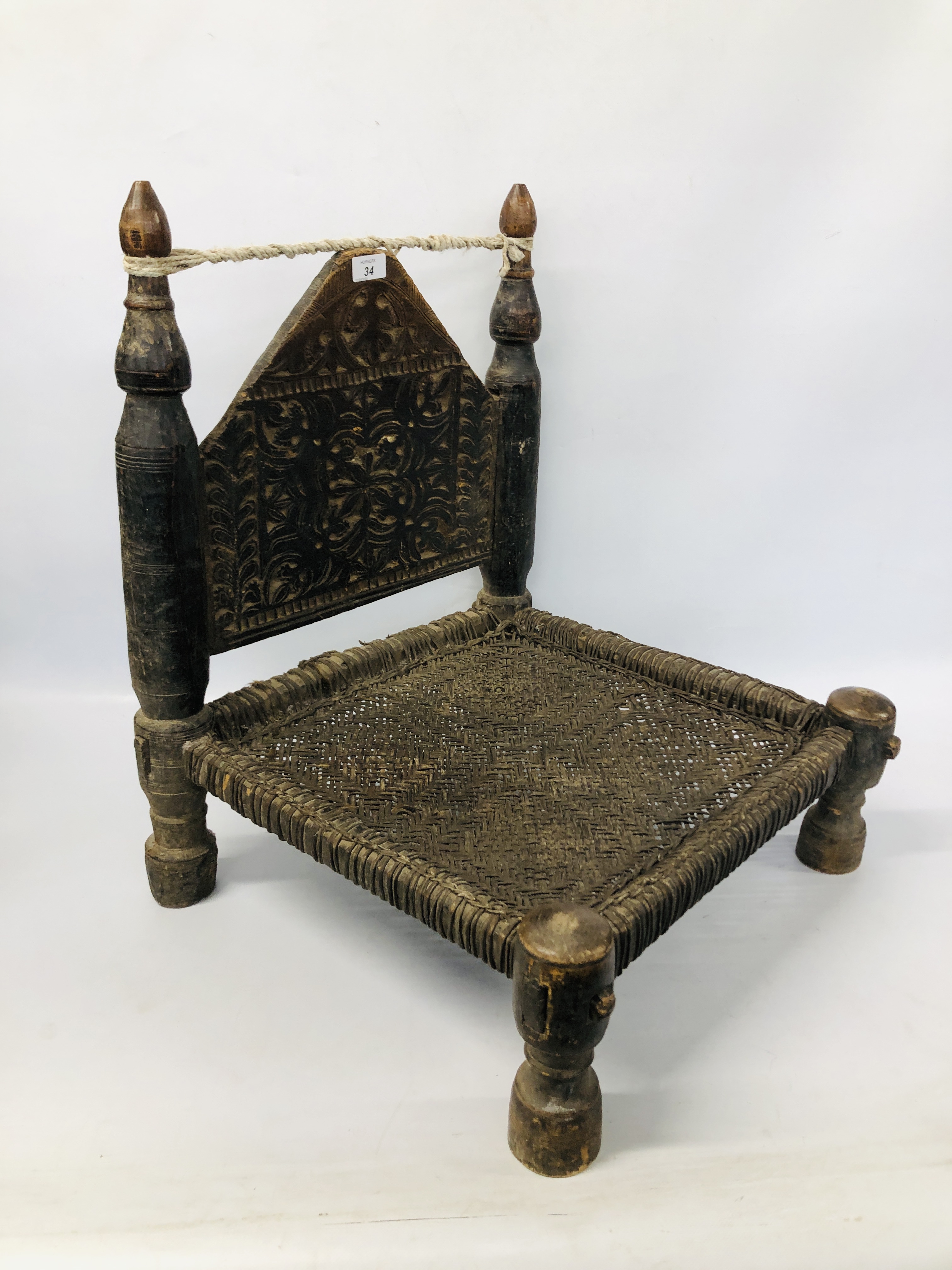 INDIAN SWAT VALLEY LOW CHAIR, THE CARVED HARDWOOD BACK ABOVE A WOVEN SEAT ON TURNED LEGS.