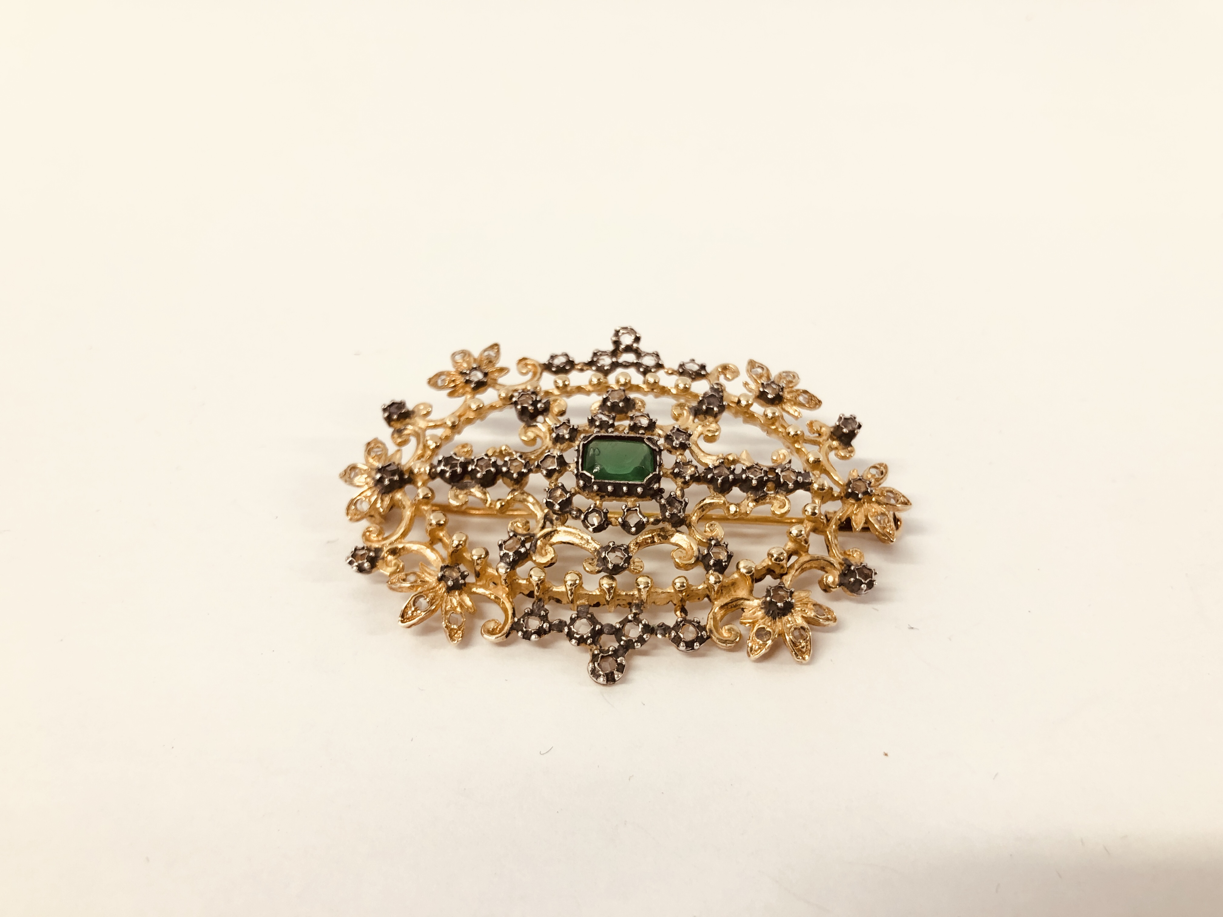 DESIGNER GILT BROOCH SET WITH CENTRAL GREEN STONE AND MULTIPLE CLEAR STONES, MARKED "ART JOY".