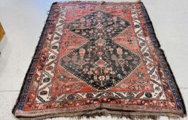 A PERSIAN RUG, THE CENTRAL DOUBLE LOZENGE FILLED WITH LEAF AND VASE MOTIF ON A BRICK RED FIELD,