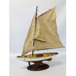 A WOODEN MODEL OF A YACHT WITH CANVAS SAILS ON DISPLAY STAND LENGTH 60CM. HEIGHT 82CM.