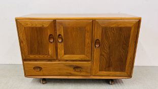 A MID CENTURY ERCOL WINDSOR THREE DOOR SINGLE DRAWER SIDEBOARD ON WHEELED CASTERS W 114CM, D 44CM,