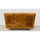 A MID CENTURY ERCOL WINDSOR THREE DOOR SINGLE DRAWER SIDEBOARD ON WHEELED CASTERS W 114CM, D 44CM,
