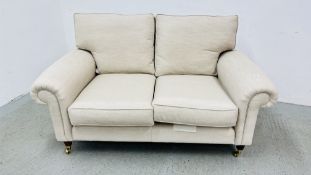 A MODERN OATMEAL UPHOLSTERED TWO SEATER SOFA STANDING ON BRASS CASTERS