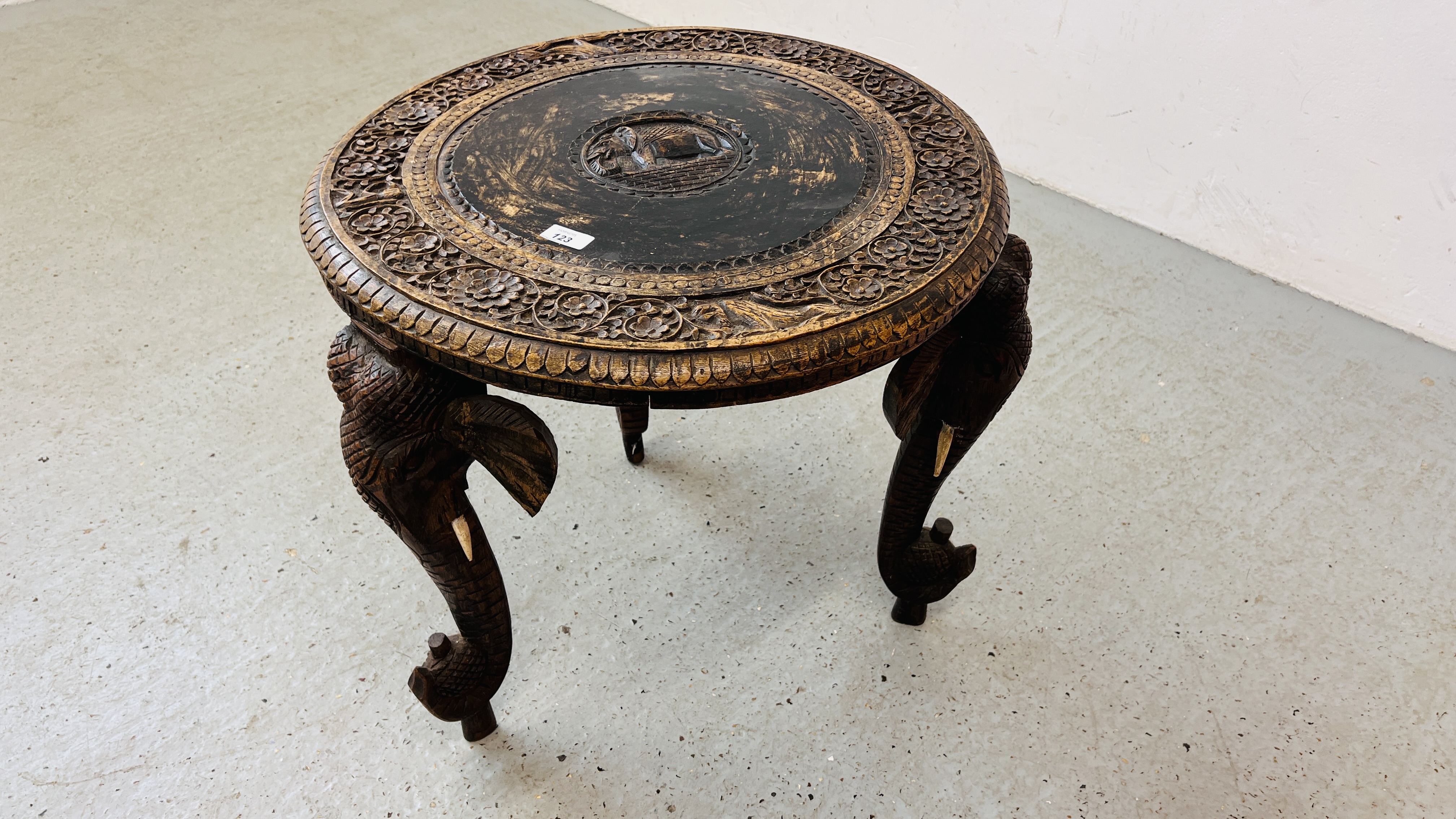 A HARDWOOD CARVED EASTERN CIRCULAR TABLE WITH ELEPHANT HEAD DETAILING TO LEGS.