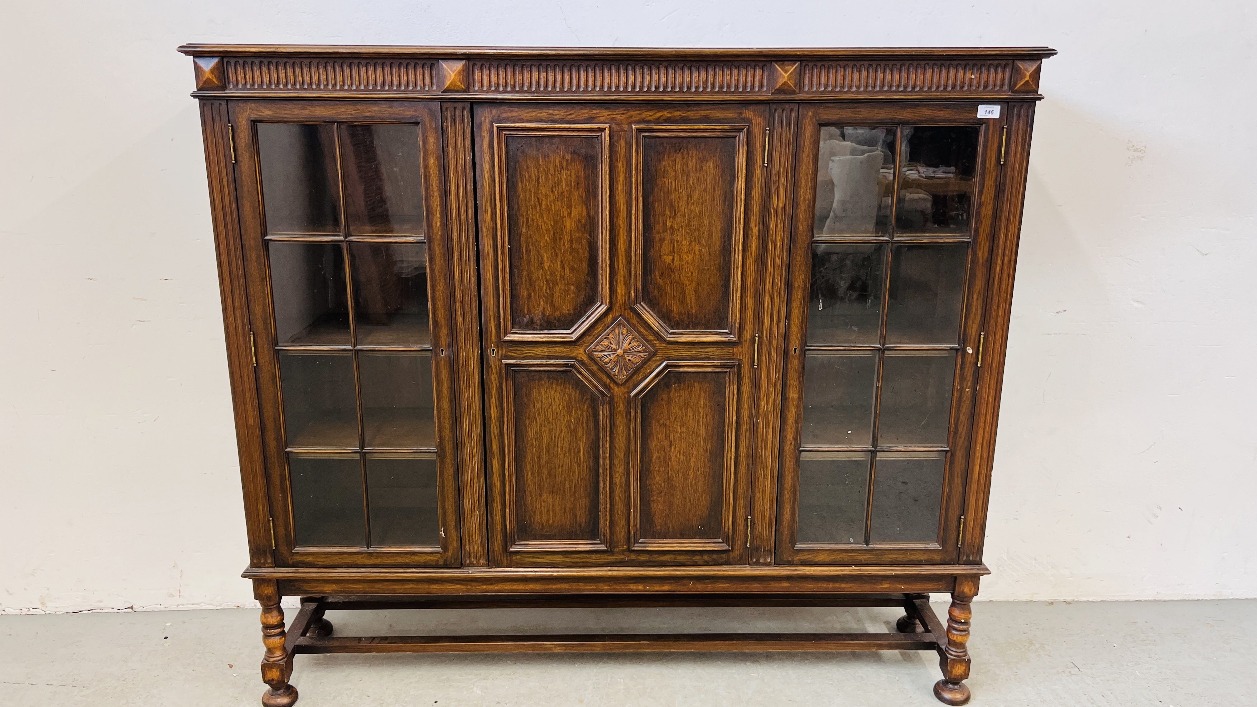 A 1930's OAK THREE DOOR CABINET STANDING ON LEG,