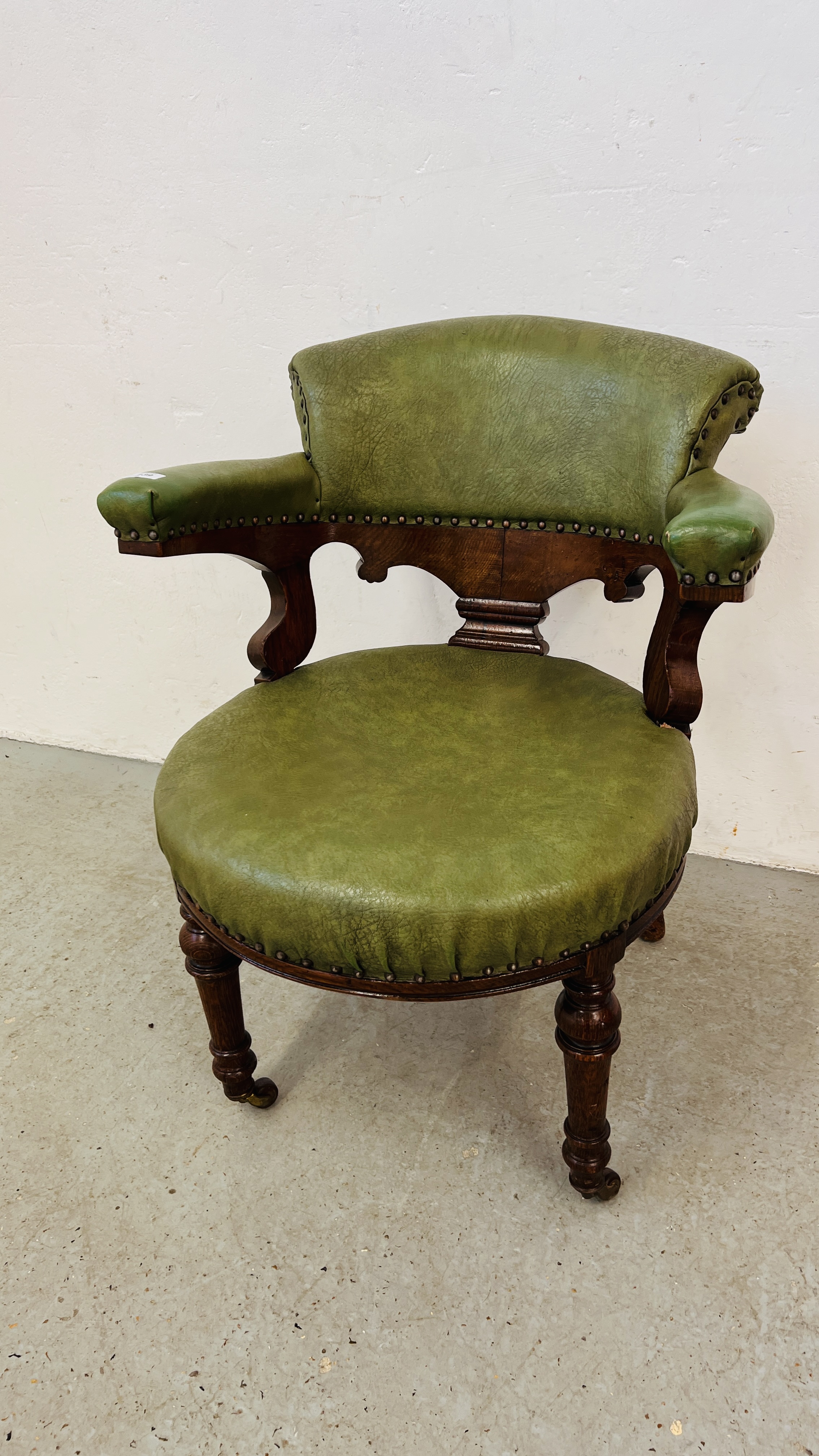 AN ANTIQUE OAK FRAMED TUB CHAIR WITH BOTTLE GREEN LEATHER UPHOLSTERY AND STUD DETAILING.