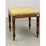 A SQUARE STOOL WITH TURNED SUPPORTS AND GOLD SILK COVER.