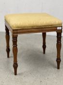 A SQUARE STOOL WITH TURNED SUPPORTS AND GOLD SILK COVER.