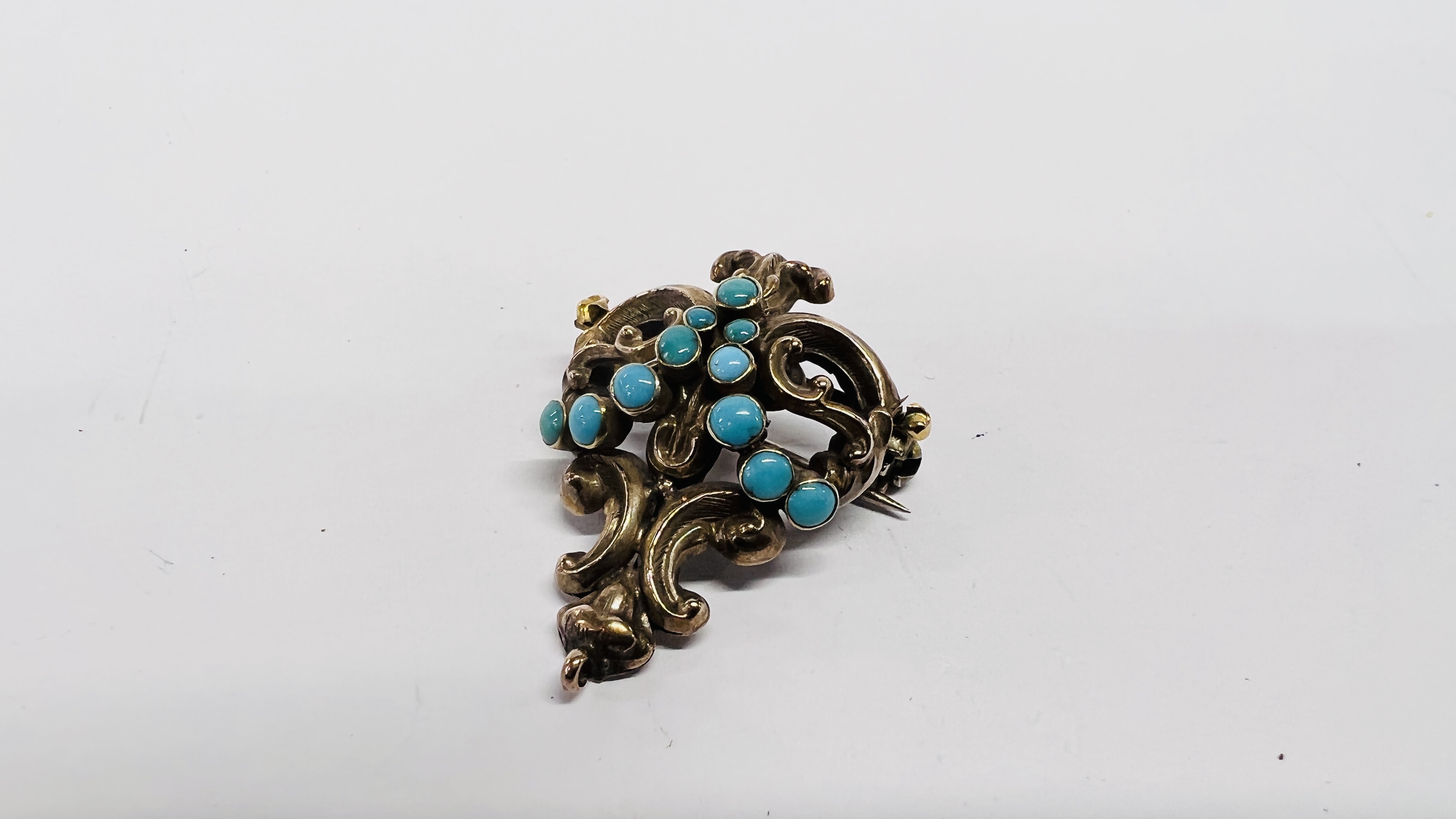 A YELLOW METAL TURQUOISE BROOCH, THE GRADUATED STONES IN A SCROLLED SETTING.
